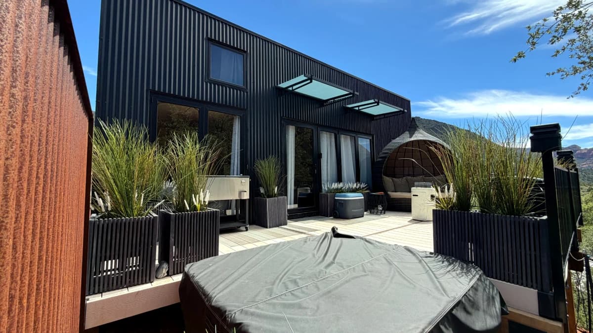 Black stacked container home with large glass doors, windows, awnings, deck, and landscaped outdoor living area