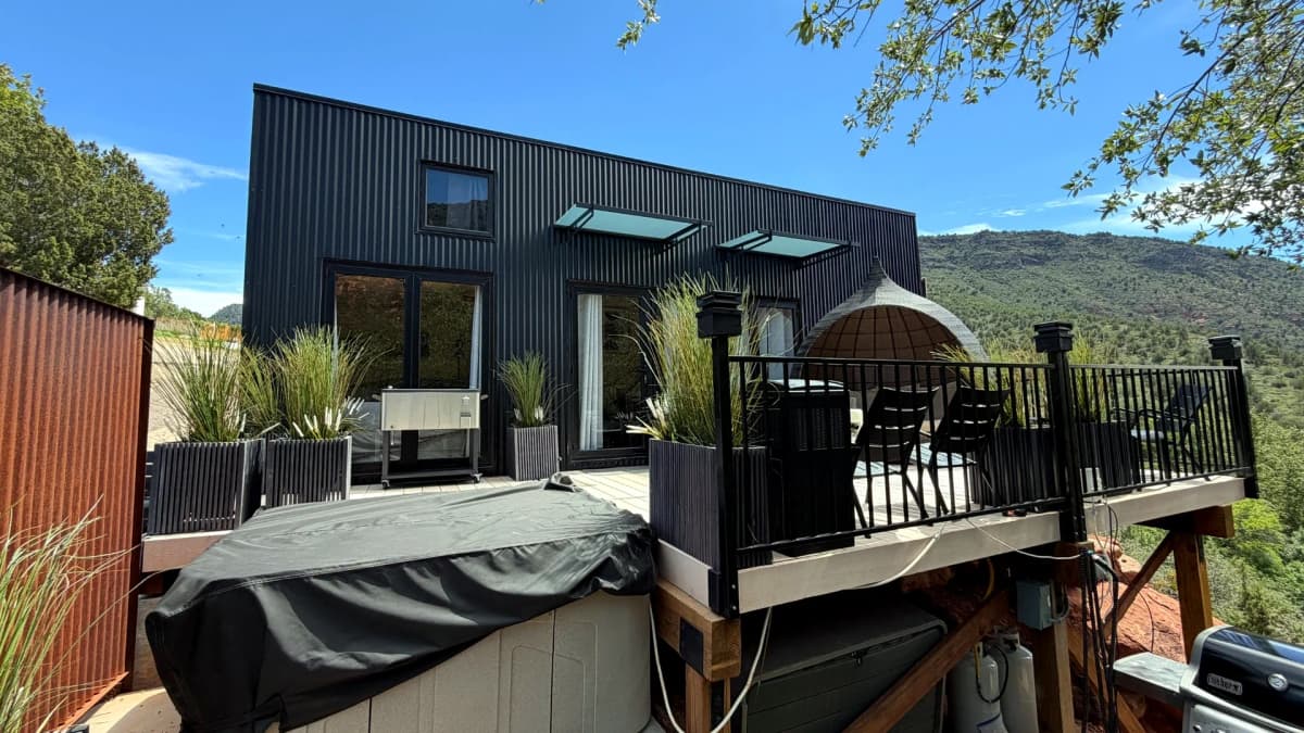 Black two-story container home with large glass doors opening onto a landscaped outdoor deck