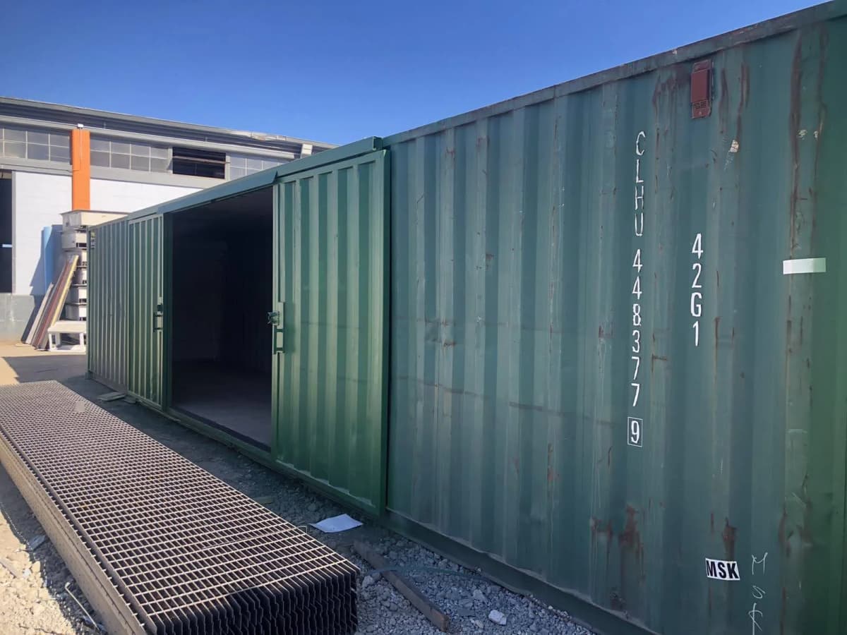 View of a shipping container with its barn doors open and corrugated flooring panels stacked outside