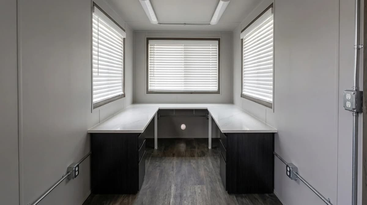 Finished D’Ambra container office interior with wraparound desk, windows, electrical outlets, LED lighting, and wood-look flooring
