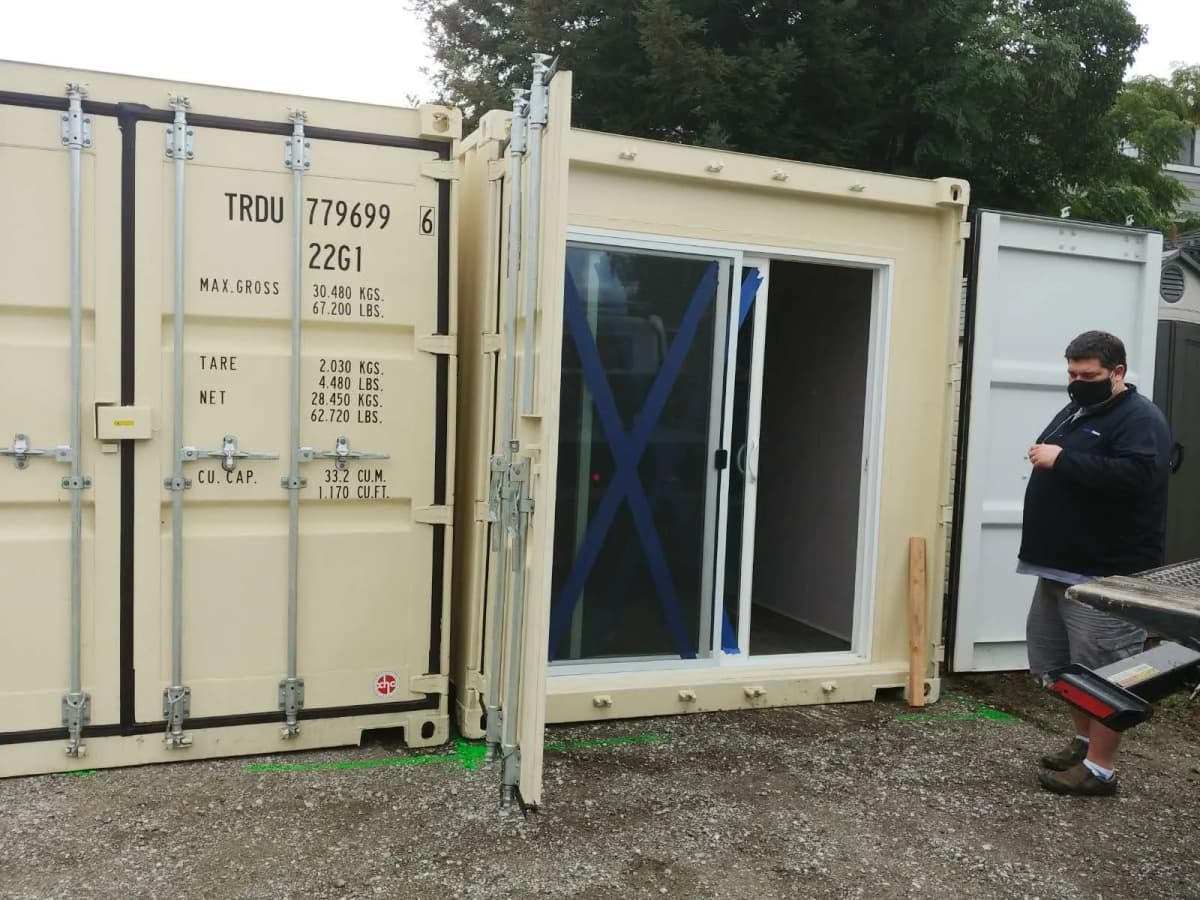 A man standing next to glass sliding doors installed behind the door of a shipping container