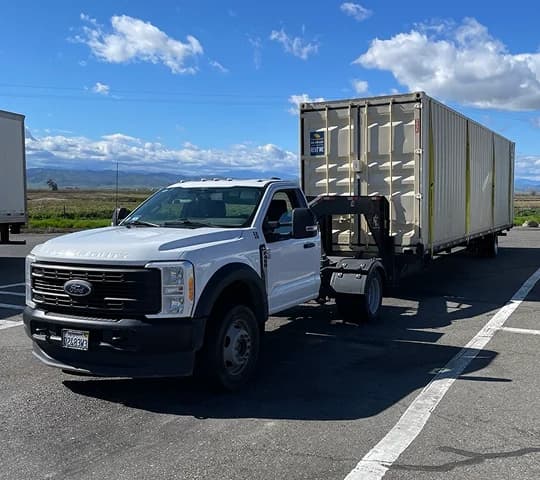 White pickup truck towing a shipping container on a trailer