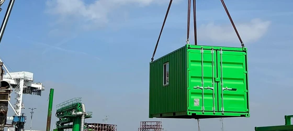 Green Conexwest container being lifted by a crane