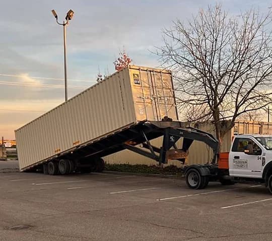 Tilt-bed truck with trailer delivering a container