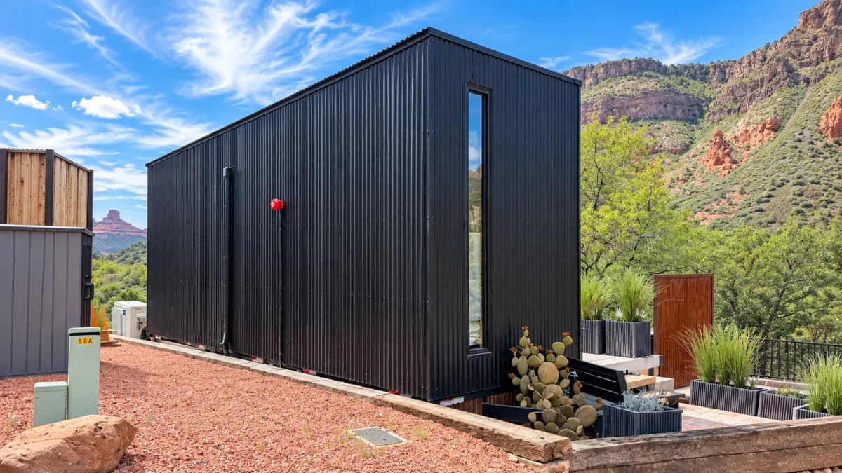 Finished black corrugated container living space installed on site with tall vertical window and landscaped outdoor area