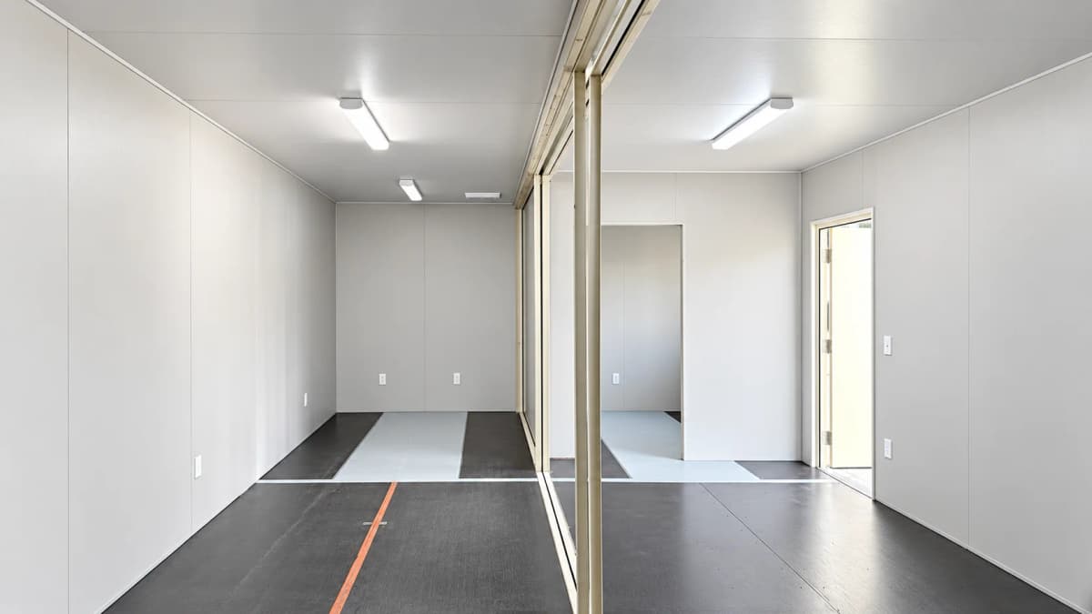 Wide finished interior of the conjoined 40ft container field office with white wall panels partitions and dark flooring