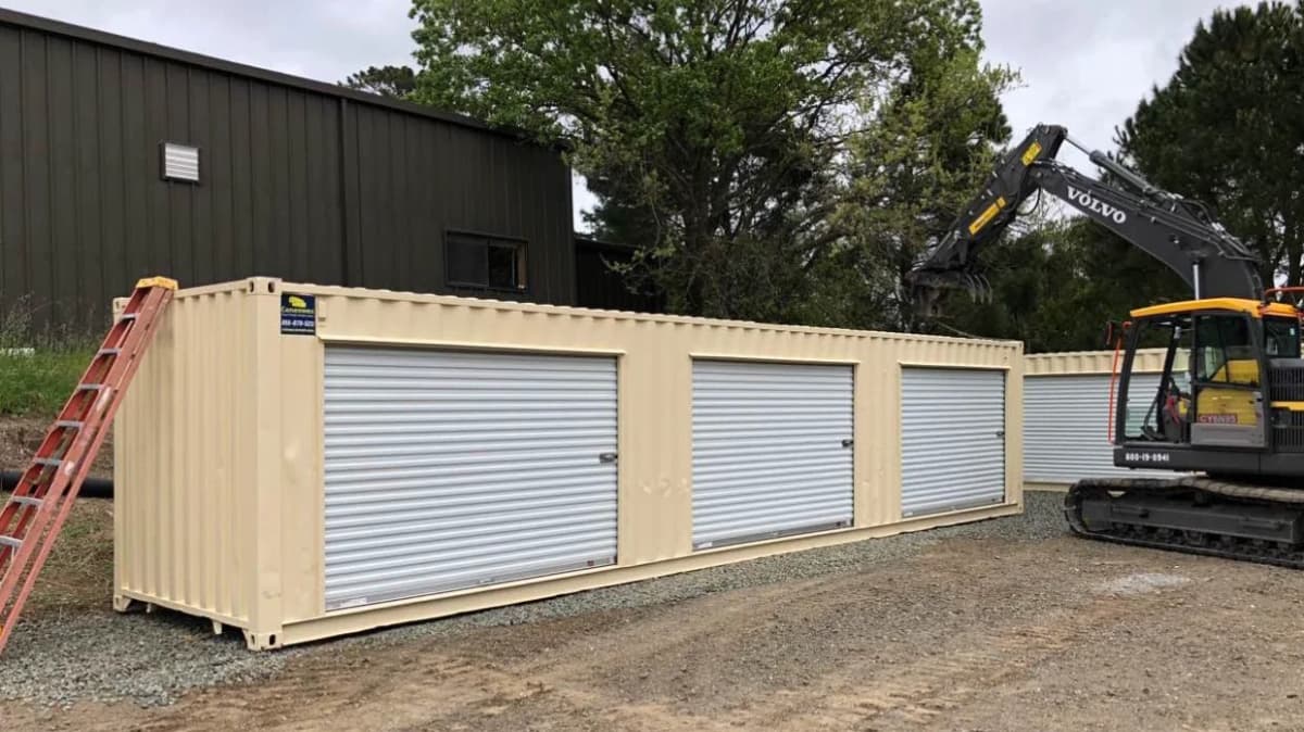 A beige modified shipping container with four roll-up garage-style doors