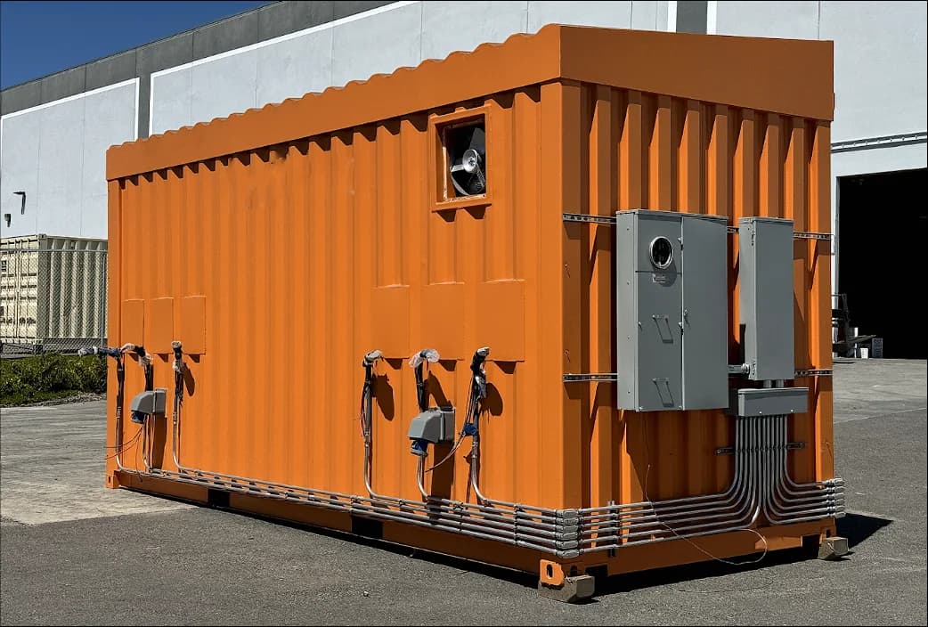 A bright orange shipping container fitted with multiple electrical panels and conduit piping on the exterior.
