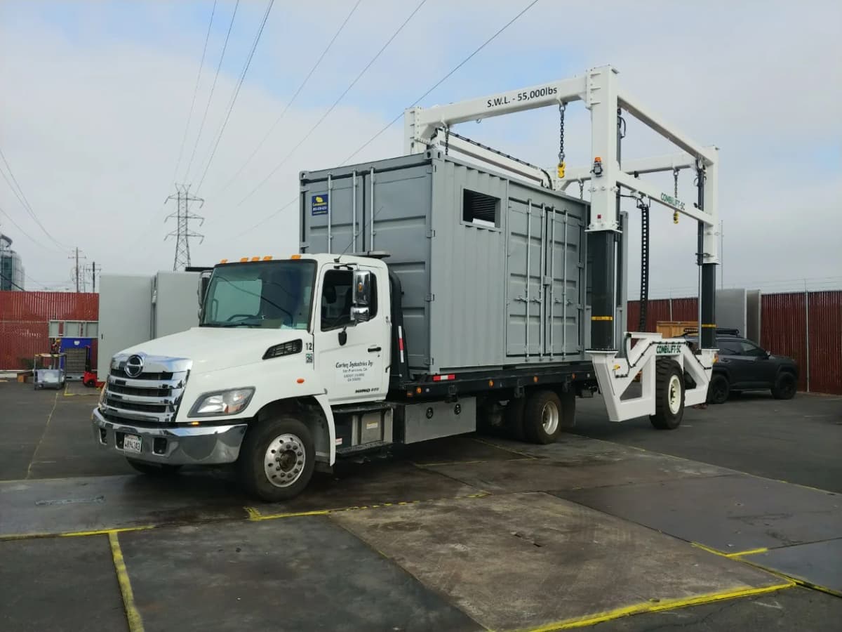 A heavy-duty white truck transporting a modified gray Conexwest shipping container.
