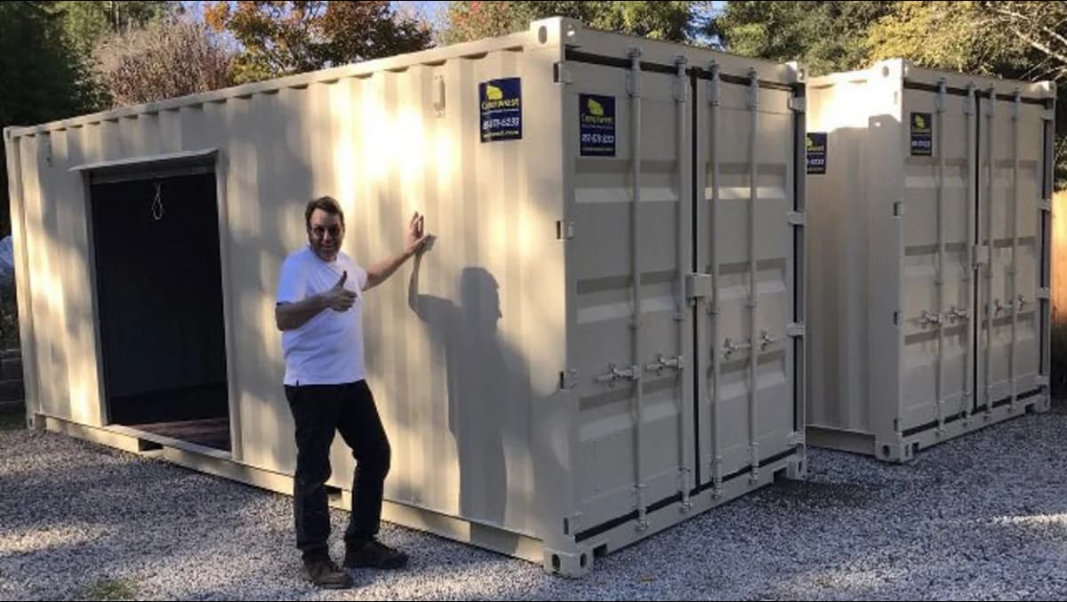 A man standing in front of two beige shipping containers.