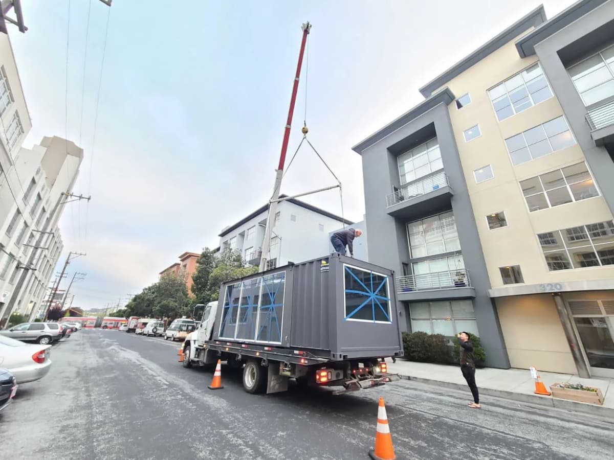 A shipping container apartment being moved by a truck.