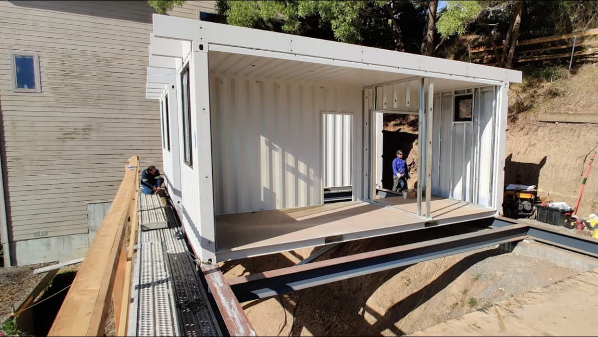 A Shipping container being converted into a modular home structure, partially built with open walls and framing.