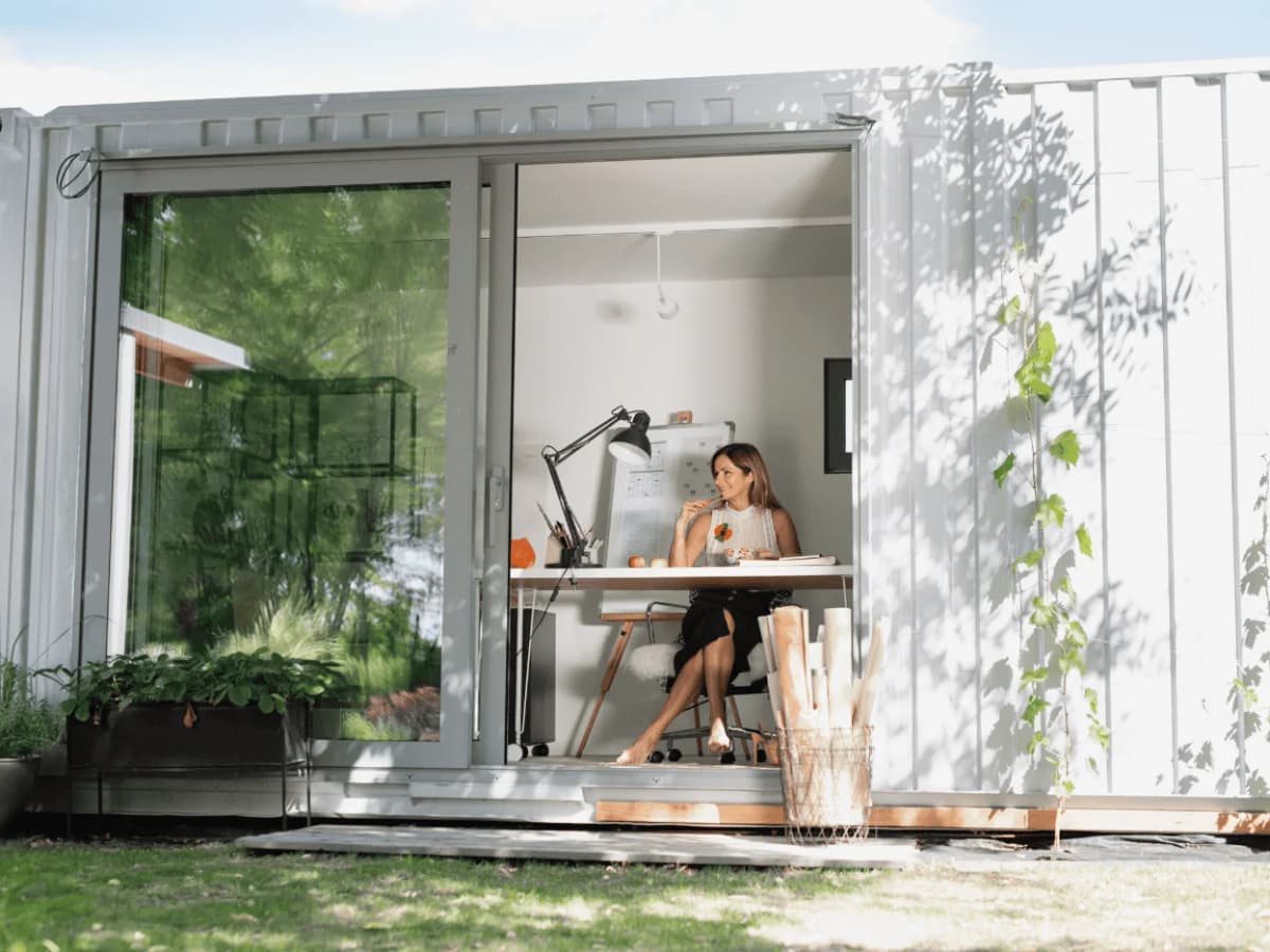 A woman working inside a modern office built from a converted shipping container with large sliding glass doors.