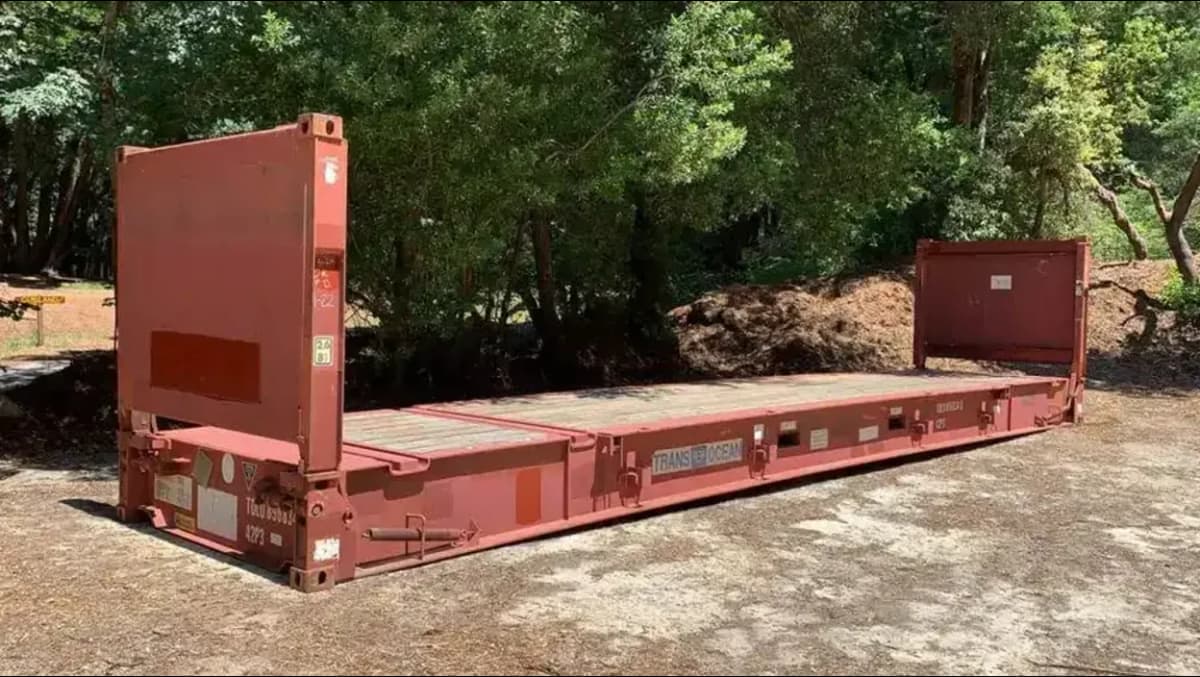 An open red shipping container in a vacant lot.