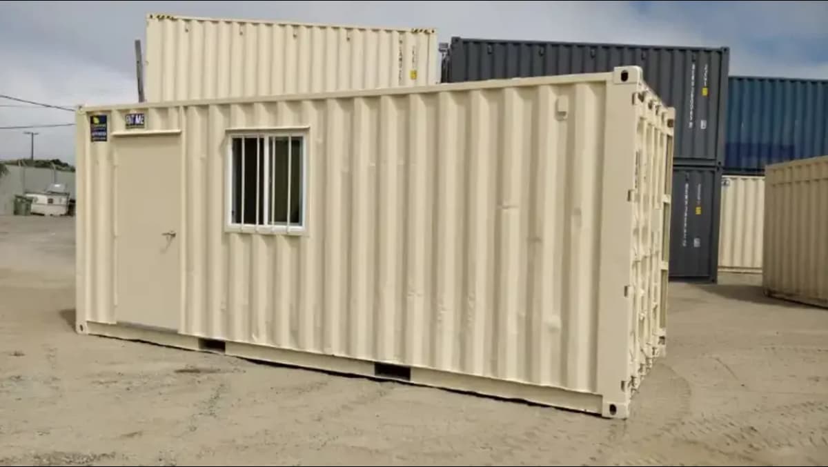 beige shipping container with a door and window in a lot.