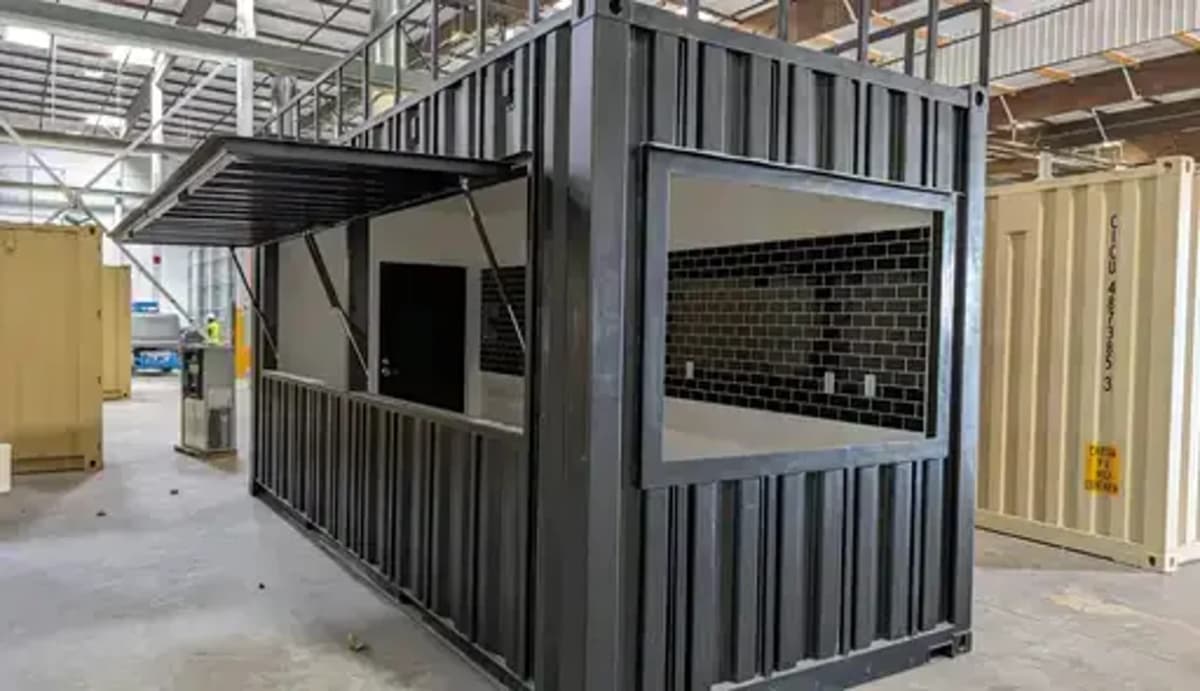 Black converted shipping container bar or cafe unit with a serving window and black tiled interior wall.