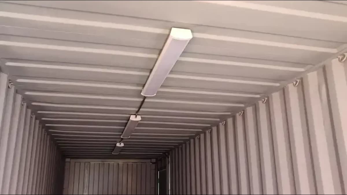 Interior ceiling of a shipping container with mounted fluorescent lighting and exposed corrugated metal walls.