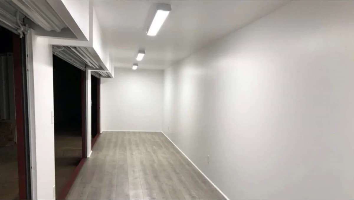Interior of a modern container unit with white walls, LED ceiling lights, and wood-style flooring.