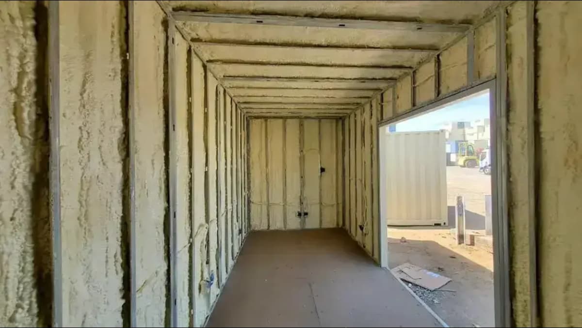 Interior view of a Conexwest shipping container being converted, with spray foam insulation applied to the walls and ceiling.
