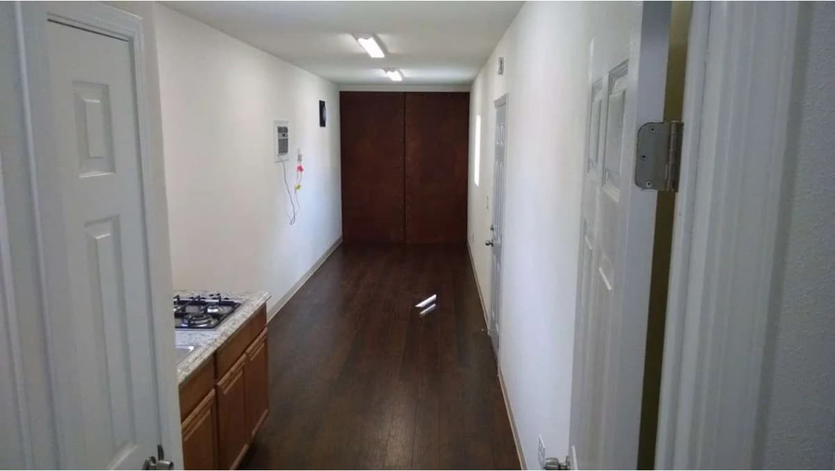 Interior view of a converted shipping container showing white walls, LED ceiling lights, and dark hardwood floors.