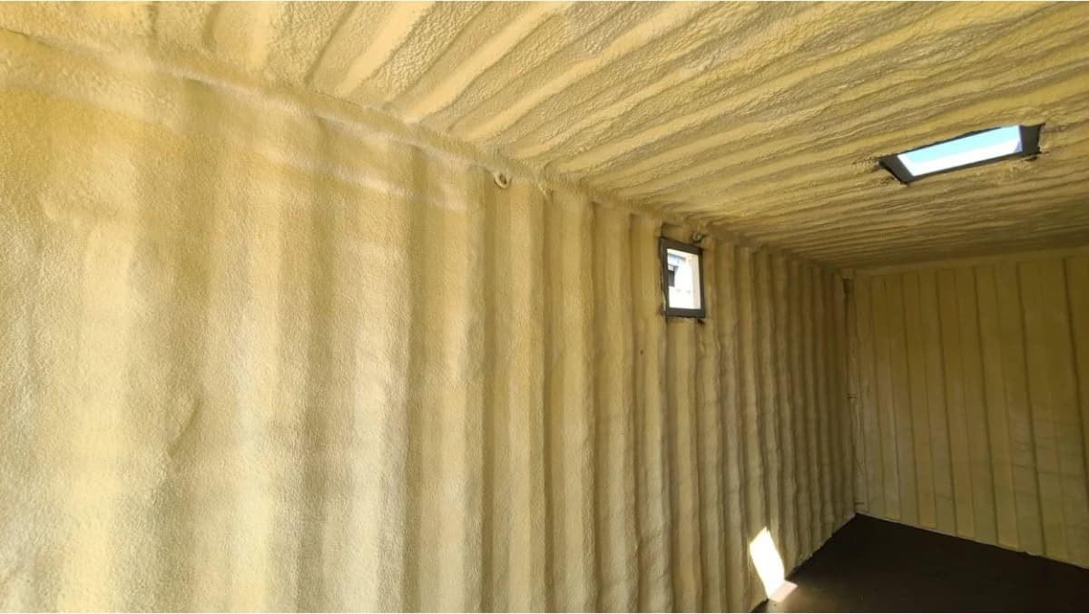 Interior view of a shipping container completely covered with yellow spray foam insulation.
