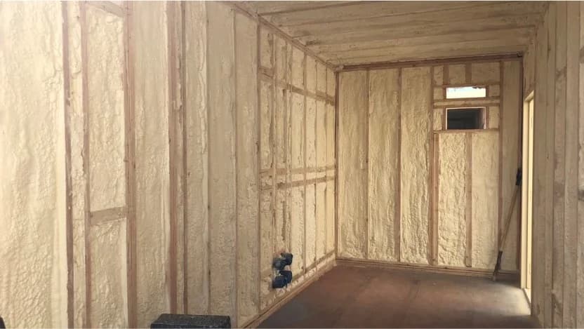 Interior view of a shipping container insulated with spray foam, showcasing wooden framing.