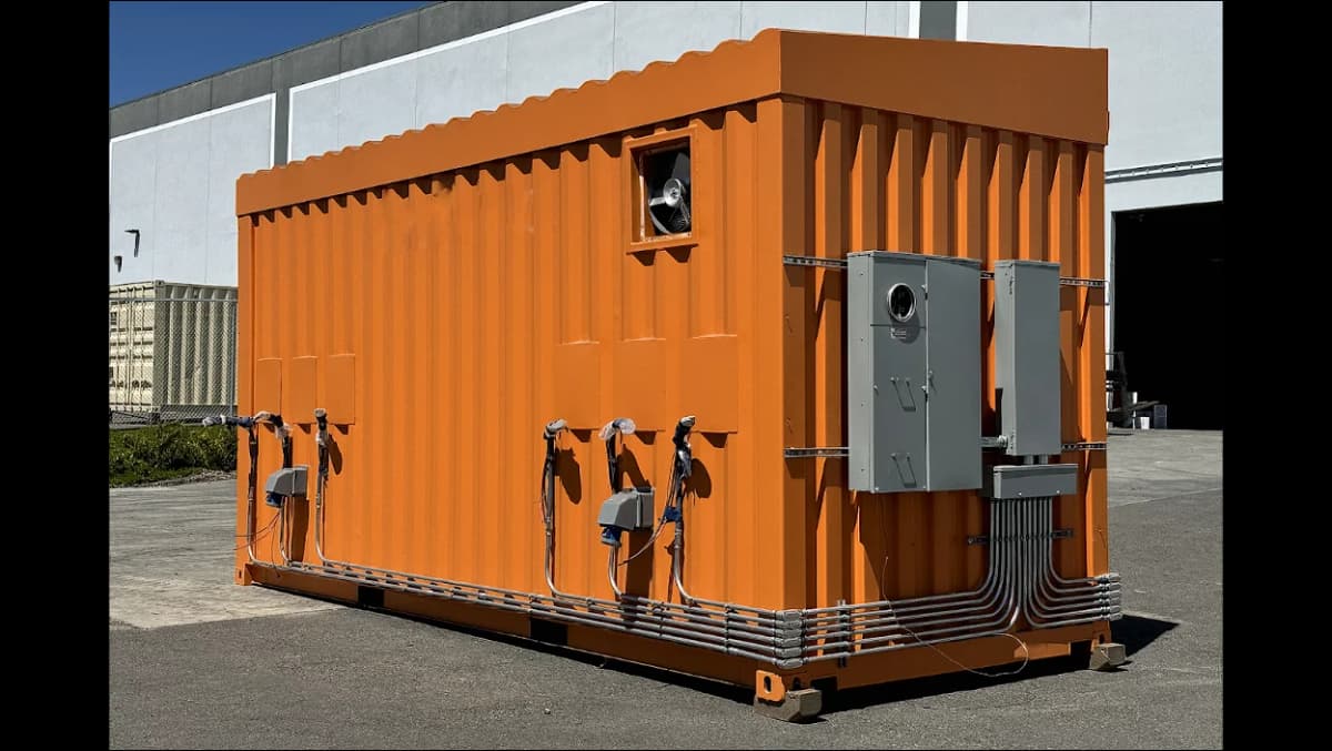 Orange shipping container with multiple electrical panels and ventilation fan installed.