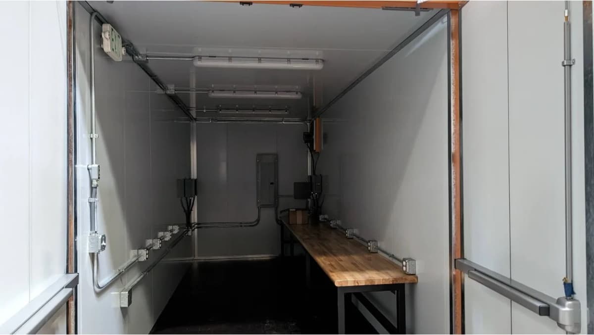 The interior of a storage container with a long desk and electrical lines.