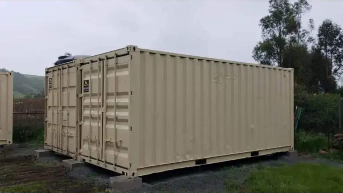 Two beige containers sitting on concrete blocks in a grassy lot.