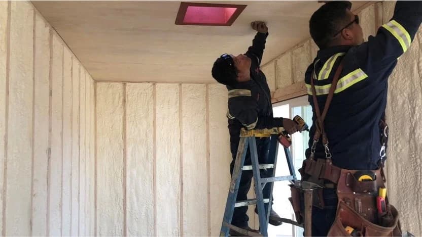 Two workers installing insulation and ceiling panels inside a container.
