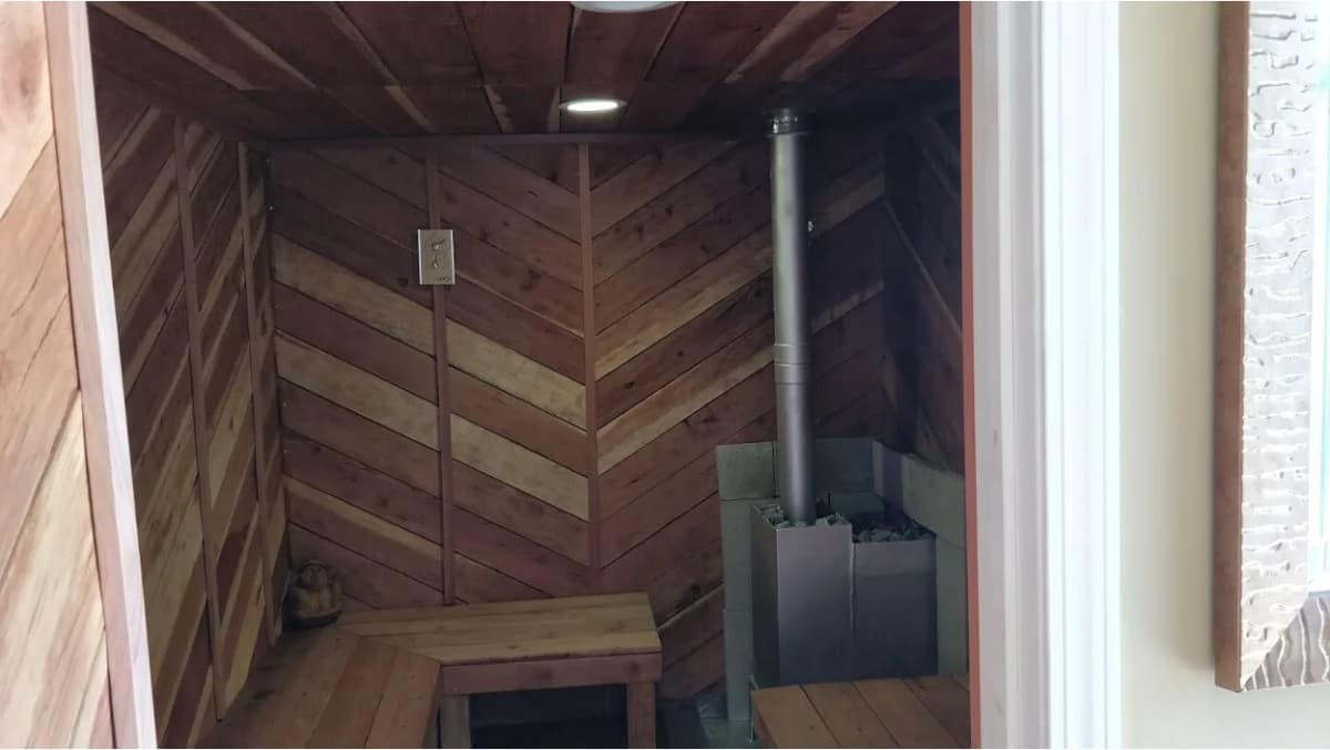 Wood-paneled sauna interior inside a container, with bench seating and a stone heater.