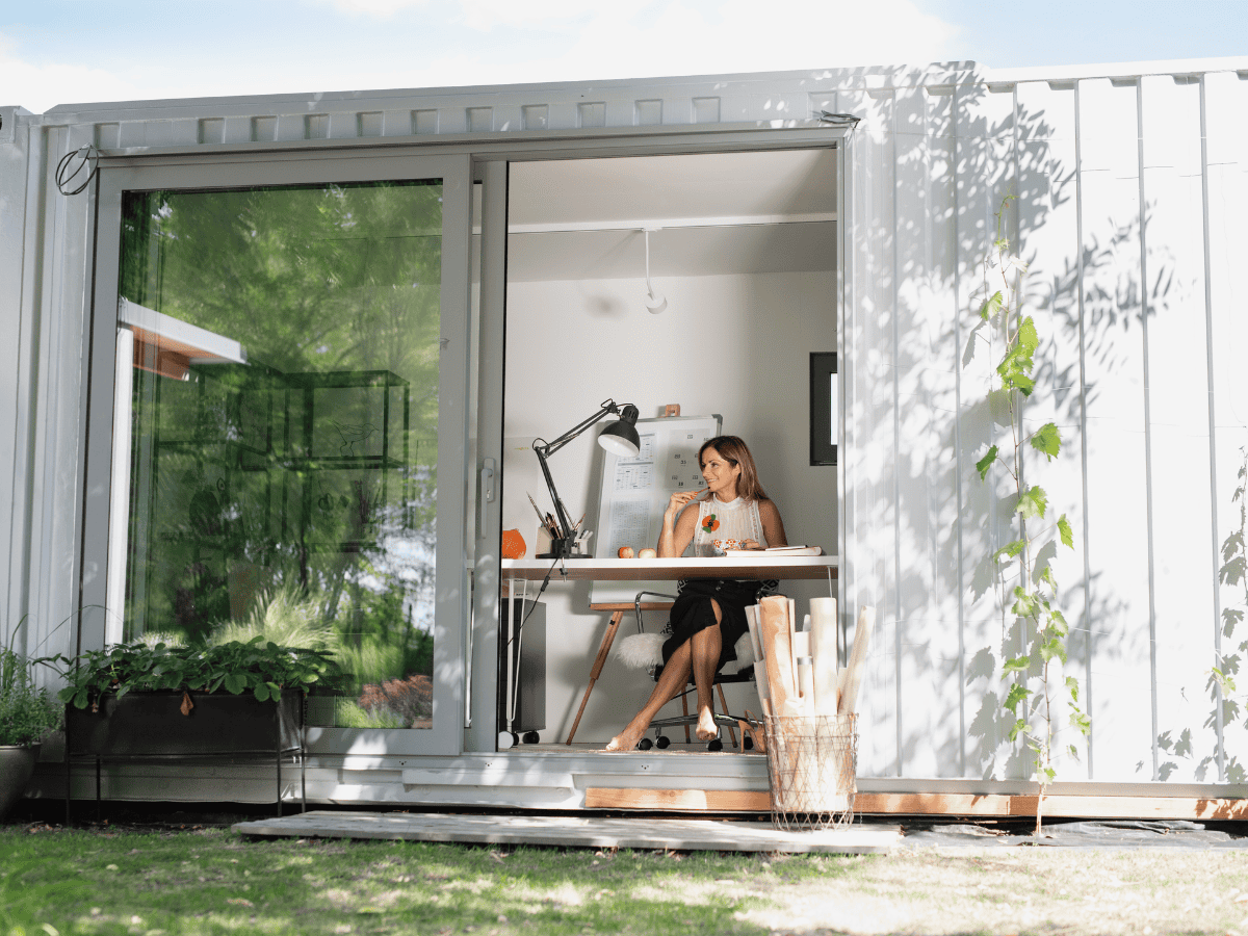 A woman working inside a modern office built from a converted shipping container with large sliding glass doors.