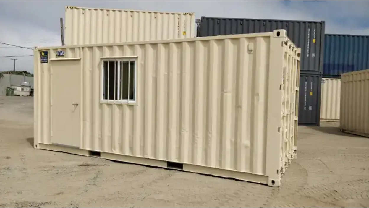 beige shipping container with a door and window in a lot.