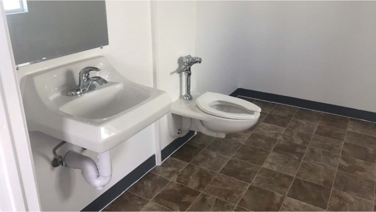 Compact bathroom interior featuring a white wall-mounted sink, toilet, and brown tile flooring.