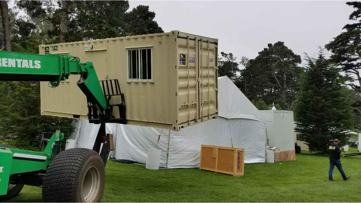 Forklift placing a modified beige shipping container with a window onto a site