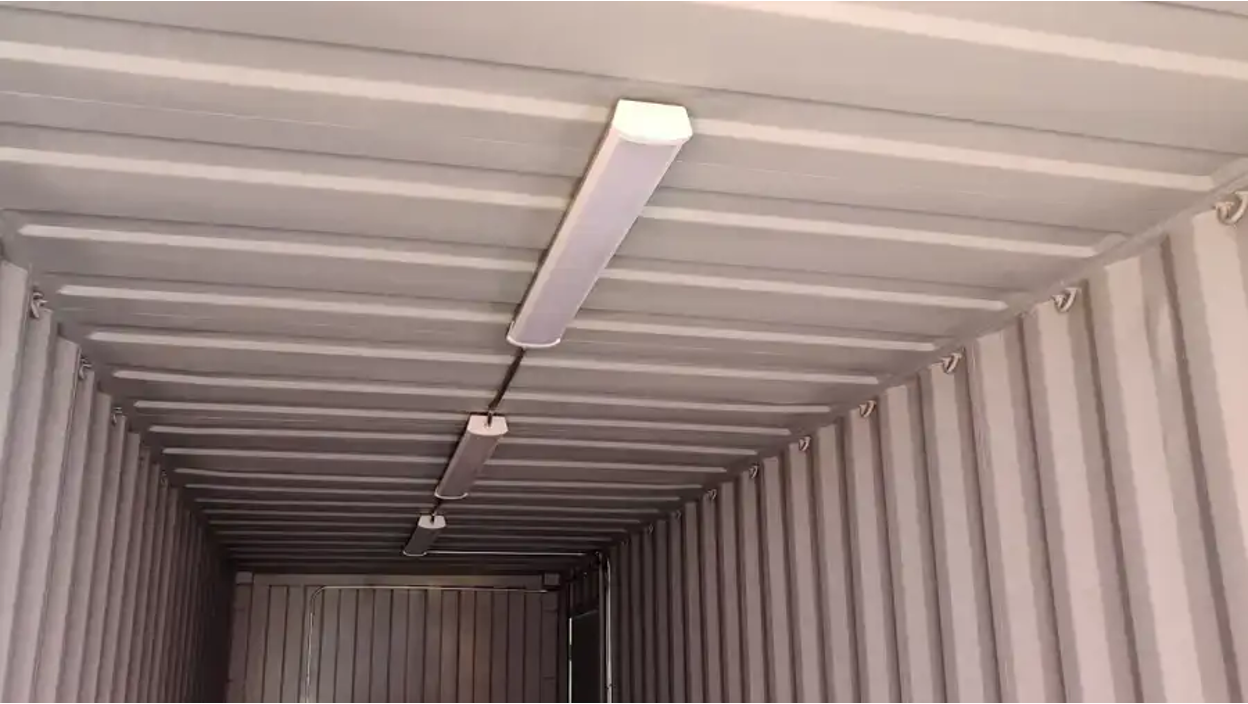 Interior ceiling of a shipping container with mounted fluorescent lighting and exposed corrugated metal walls.