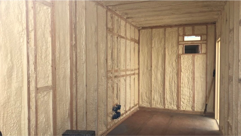 Interior view of a shipping container insulated with spray foam, showcasing wooden framing.