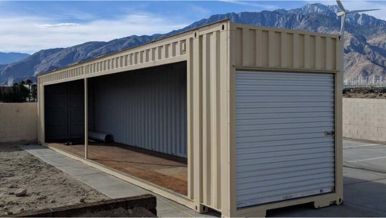 Modified beige shipping container with roll-up door and open side.