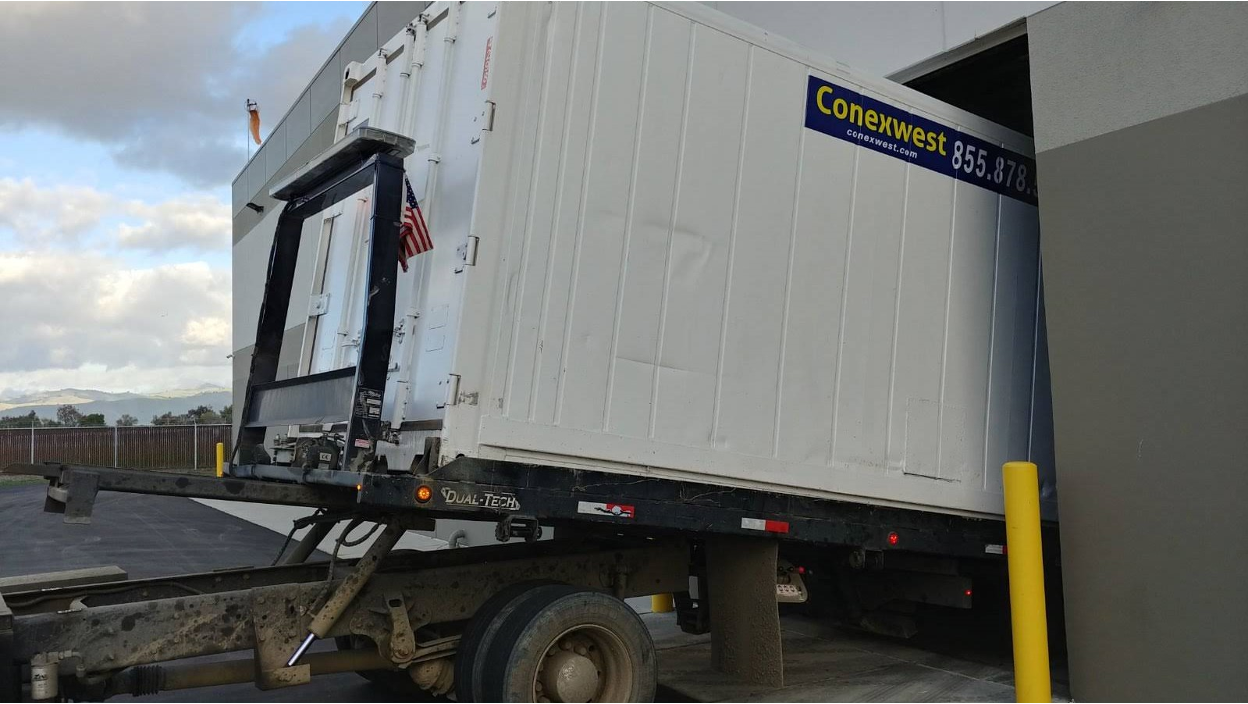 White Conexwest shipping container being unloaded from a delivery truck.