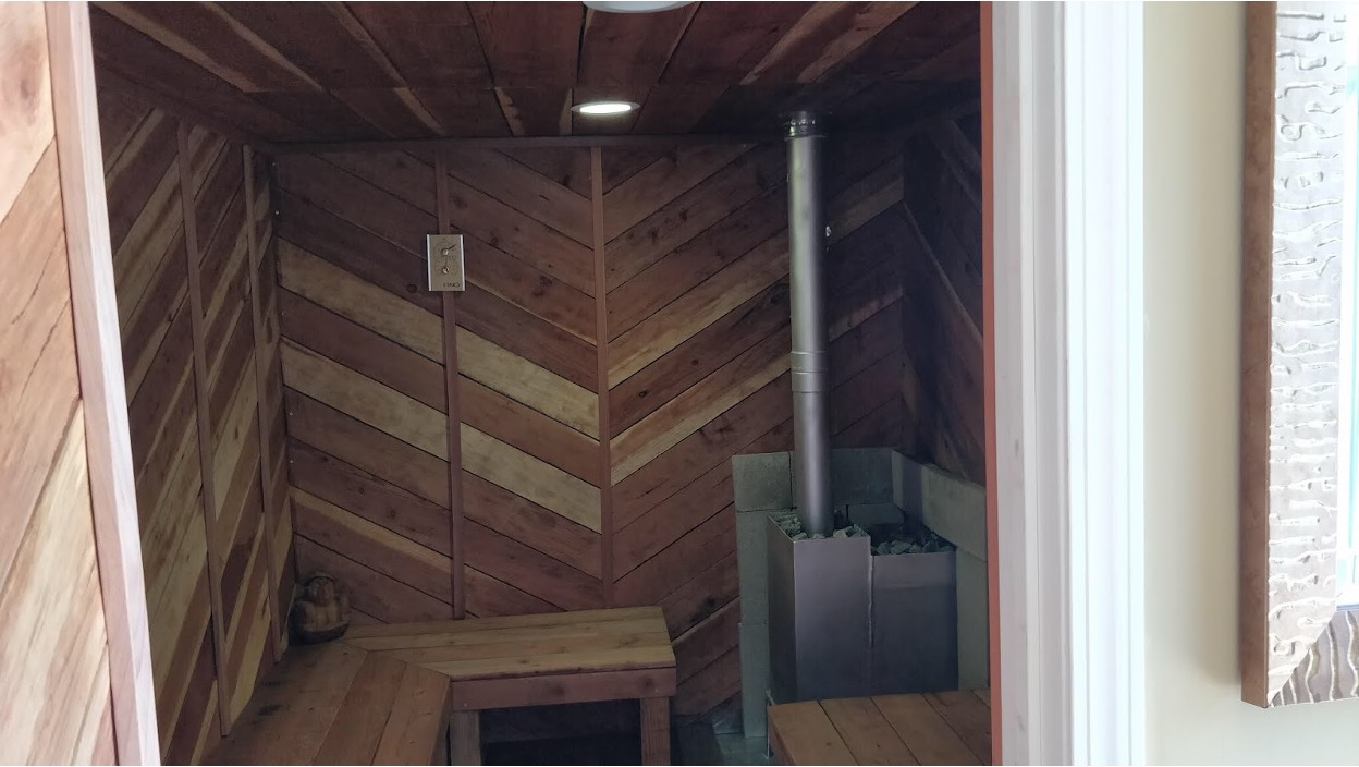 Wood-paneled sauna interior inside a container, with bench seating and a stone heater.